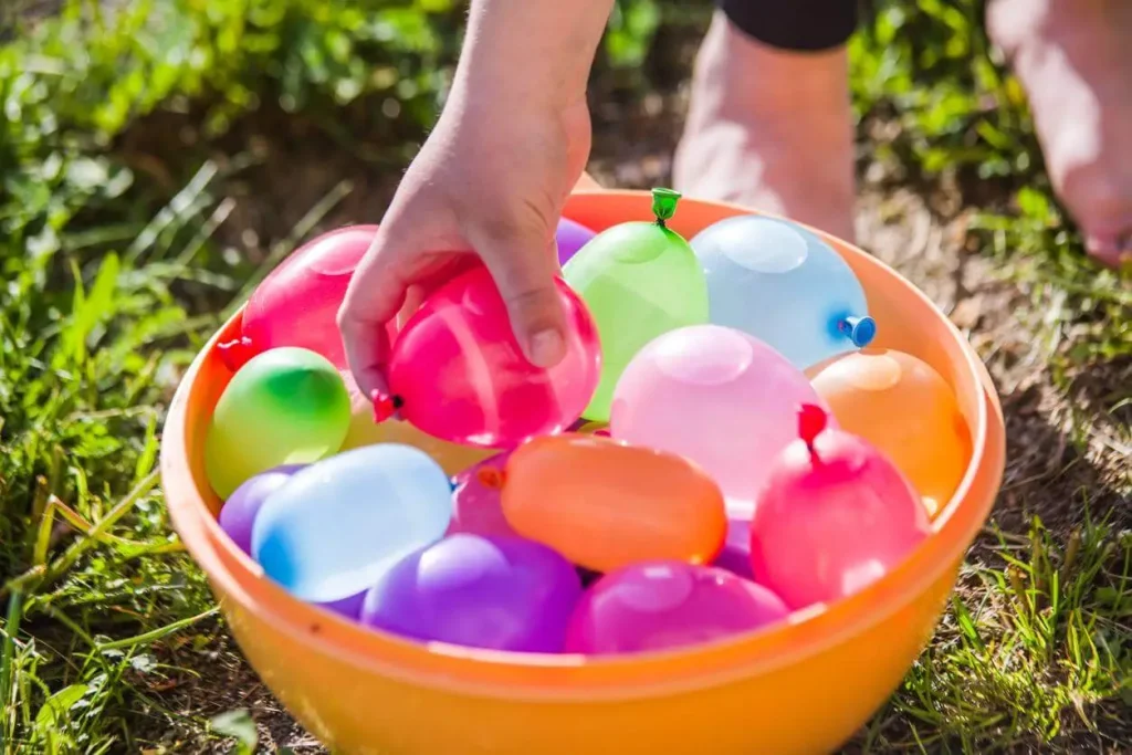 Bacia com várias bexigas cheias de água e uma pessoa pegando uma delas