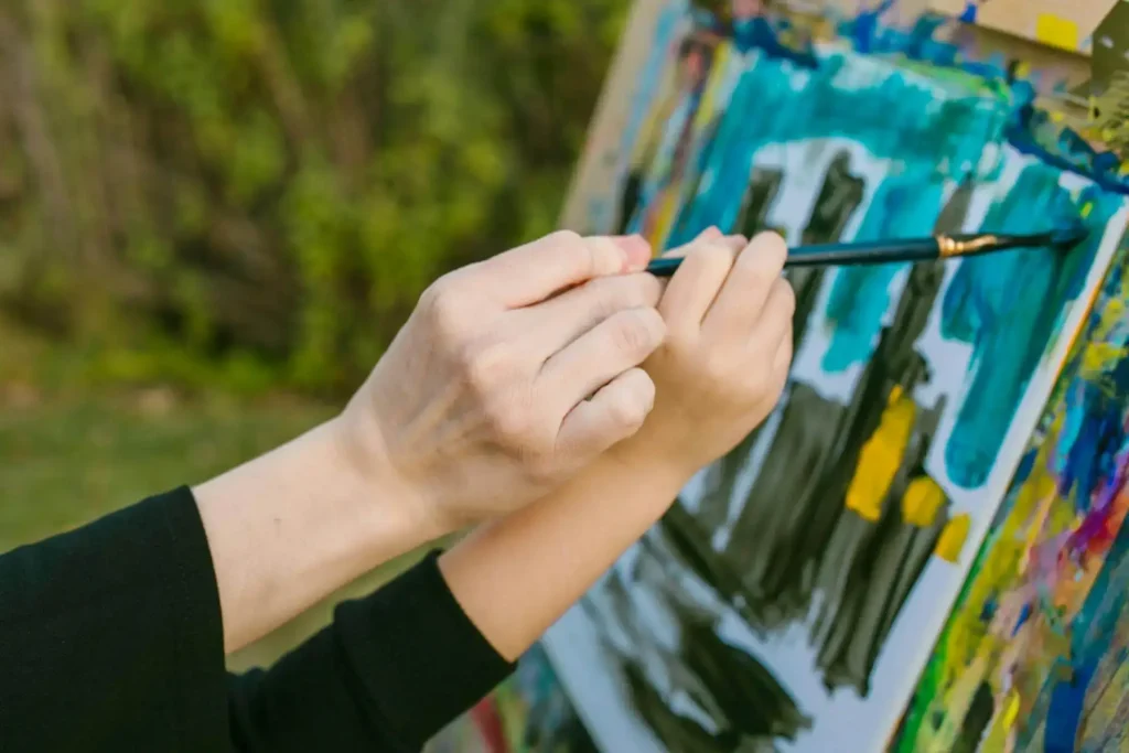 Mãos pintando um quadro com desenho abstrato de uma paisagem de cidade